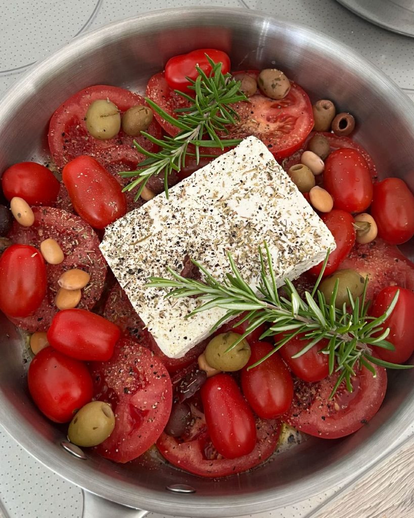 Tomate et tomates cerises dans une sauteuse avec un bloc de feta et du romarin